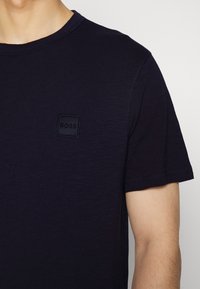 Navy blue short-sleeve t-shirt made of textured fabric with a round neck, featuring a small black "BOSS" logo patch on the chest.