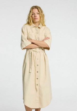 Beige skjorte kjole med korte ærmer, belted midje og to brystlommer; lavet af et glat, let stof.