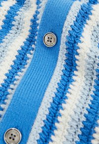 Gestickte blau-weiße Strickjacke mit horizontalen Streifen und gerippten Details, mit einem runden silbernen Knopf in der Mitte.