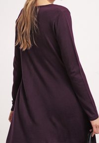 Robe longue à manches longues de couleur violette avec une coupe décontractée, réalisée en tissu doux. Elle présente un col rond et une silhouette fluide, se terminant au-dessus des genoux.