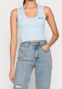 Ljusblå ribbad kort topp med rundad halsringning och liten "BDG JEANS"-logotyp, tillsammans med slitna ljusblå högmidjade jeans.