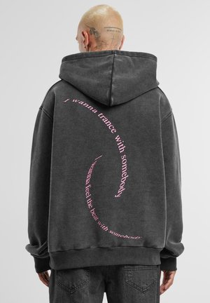 Oversized dunkelgrauer Hoodie mit einem großen, rosa, kreisförmigen Textdesign auf der Rückseite, das Slogans über das Verlangen nach Trance und das Gefühl des Beats enthält.