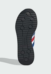 Semelle de sneaker en caoutchouc noir avec des rainures de traction et cinq motifs de grip circulaires ; présente un logo en relief au centre.