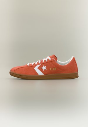 Lågprofil orange mockasinsneaker med vita snören, vit stjärna och pil-logotyp, texten "All Star" och brun gummisula.