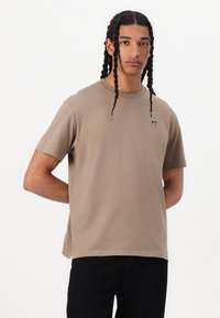 Kortærmet beige bomulds t-shirt med rund hals, prydet med et lille emblem på venstre bryst og en afslappet pasform.
