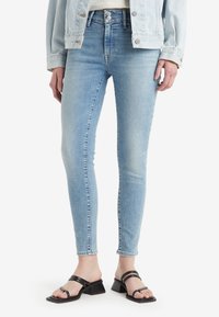 Ljust blå skinny jeans har hög midja, subtila blekningar och klassisk femfickorsdesign, som kombineras med svarta sandaler med remmar.