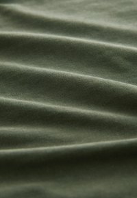 Tissu en coton vert olive avec une texture lisse, présentant de doux plis et des variations subtiles de couleur. Idéal pour les vêtements ou la tapisserie.