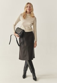 Brauner Leder-Midirock mit geradem Schnitt, kombiniert mit einem cremefarbenen Rollkragenpullover. Hält eine schwarze Umhängetasche mit langem Riemen.
