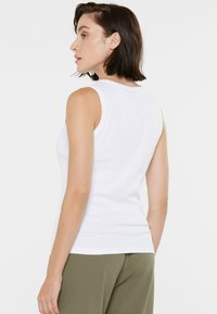 White sleeveless top made of ribbed fabric, featuring a round neckline and a fitted design, paired with light olive green pants.