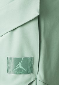 Lichtgroene sportkleding met een gladde textuur. Voorzien van een gestikte label met een Jumpman-logo en het woord "Flight".