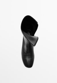 Černá kožená kotníková bota s kulatou špičkou a hladkým povrchem, která má otevřenou horní část a minimalistický design.