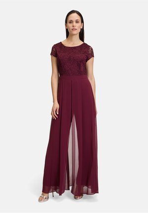 Abito borgogna con corpo in pizzo, maniche corte e gonna in chiffon plissettata con spacco frontale. Sandali argento completano l'outfit.