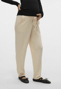 Ljust beige, mjukt tyg, avslappnade byxor med dragsko i midjan och sidofickor, kombinerat med svarta platta skor med sländor.