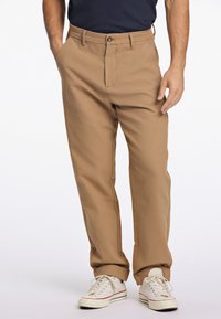 Beige bomullbyxor har en avslappnad passform, raka ben, sidfickor och stängs med en metallknapp, parat med vita sneakers.