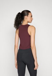 Burgundy crop tank top with a round neckline and sleeveless design, paired with high-waisted black leggings, smooth texture.