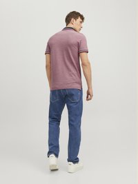 Polo skjorte i burgunderrød stof, kortærmet med marineblå krave og stribede accenter. Sat sammen med blå jeans og hvide sneakers.