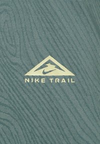 Nike Trail fabric features a textured pattern in teal, with a gold triangular logo and bold text reading "NIKE TRAIL" underneath.