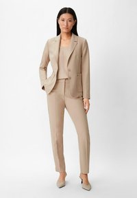 Jasnobeżowy garnitur składający się z dopasowanej marynarki z dwoma guzikami, pasujących zwężających się spodni oraz prostego topu, wszystko w gładkiej, tkanej tkaninie.