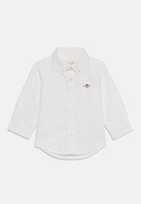 White long-sleeve shirt made of cotton. Features a button-down collar, front buttons, and a small embroidered logo on the chest. Rounded hem.