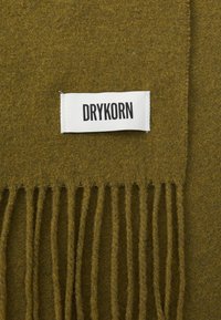 Sciarpa frangiata verde oliva realizzata in materiale morbido, con un'etichetta bianca su cui è scritto "DRYKORN" in neretto nero.