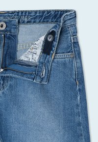 Modré džíny z denimu s zipovým zipem, knoflíkovým zapínáním a několika kapsami s bledým mácháním. Na látce jsou viditelné opotřebené detaily.