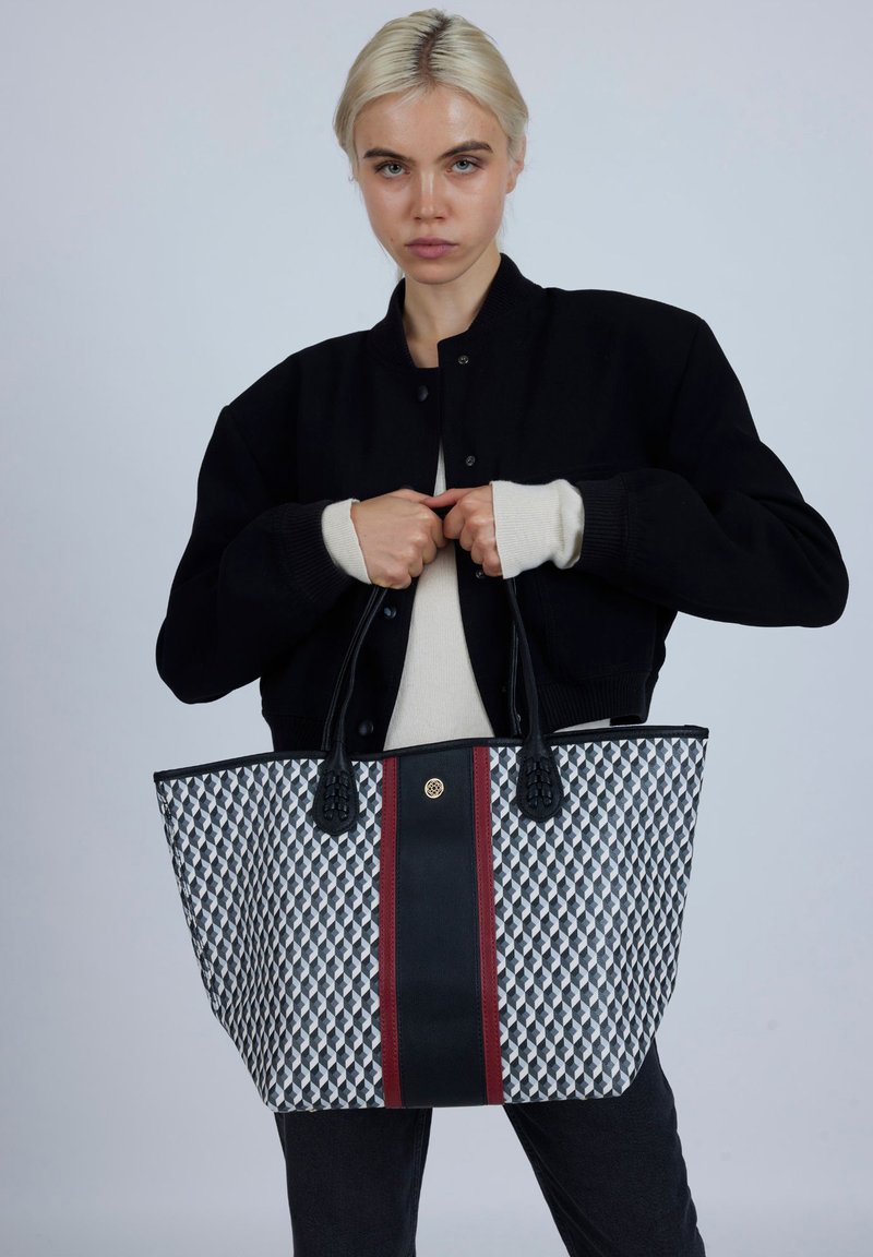 Czarna torba typu tote z geometrycznym wzorem w odcieniach szarości i bieli, czarnym paskiem pośrodku oraz teksturowanymi czarnymi uchwytami.