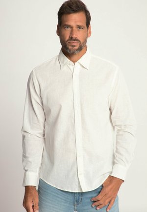 Camicia bianca a maniche lunghe in lino con colletto a punta, patta con bottoni e orlo leggermente curvo. Indossata con jeans in denim azzurri.