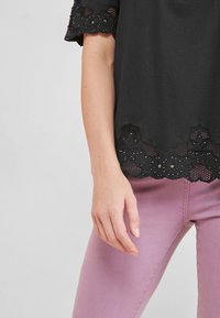 Haut noir avec détail en dentelle à l'ourlet, présentant des motifs floraux et de petites décorations ; assorti à un pantalon rose clair.