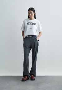 Valge Moschino T-särk musta trüki ja hallide pükste, millel on bränditud vöökoht, koos marooni värvi kingadega. Siledad tekstuurid.