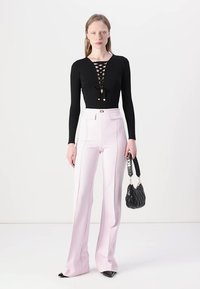 Top preto de manga longa com detalhe de cordão na frente, combinado com calças rosa claro de perna larga. Modelo leva uma pequena bolsa preta acolchoada.