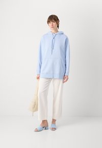 Felpa oversized azzurra con tasca frontale, abbinata a pantaloni bianchi a gamba larga e sandali con tacco blocco azzurri.