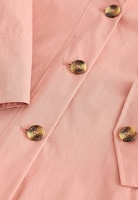 Light pink fabric coat with a smooth texture, featuring large round buttons with a marbled pattern and subtle stitching details.