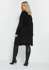 Abito maglione nero in maglia morbida con vestibilità ampia, maniche lunghe, spacchi laterali e orlo arrotondato, abbinato a stivali neri in pelle al ginocchio.