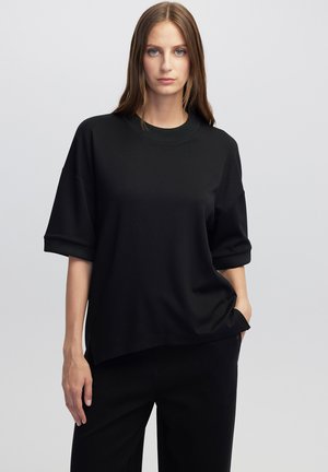 Černá oversized mikina s krátkým rukávem a kulatým výstřihem, vyrobená z hladkého materiálu, s volným střihem a bočními rozparky.