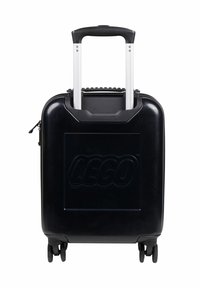 Valigia rigida nera con un logo LEGO evidente, manico telescopico in alluminio, ruote scorrevoli e accenti testurizzati sulla parte superiore.