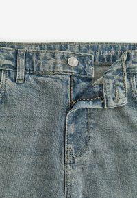 Jean en denim bleu clair avec une coupe slim. Texture déchirée, fermeture à bouton standard et fermeture éclair fonctionnelle à l'avant.