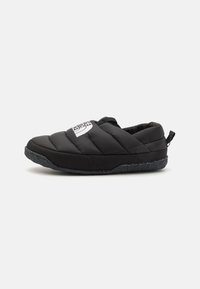 Scarpe slip-on nere trapuntate con una parte superiore imbottita, caratterizzate da un logo bianco sul davanti e una suola in gomma testurizzata con dettagli maculati.