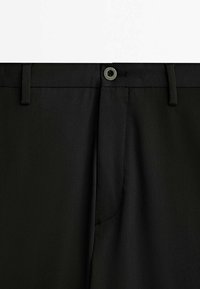 Mustat housut sileällä pinnalla, joissa on napillinen kiinnitys, vyölenkit ja sivutasku. Yksinkertainen muotoilu, suora leikkaus.