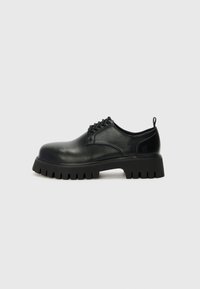 Chaussures en cuir noir à lacets avec un bout arrondi, semelle en caoutchouc texturé et une petite languette au niveau du talon. Comprend six œillets pour les lacets.