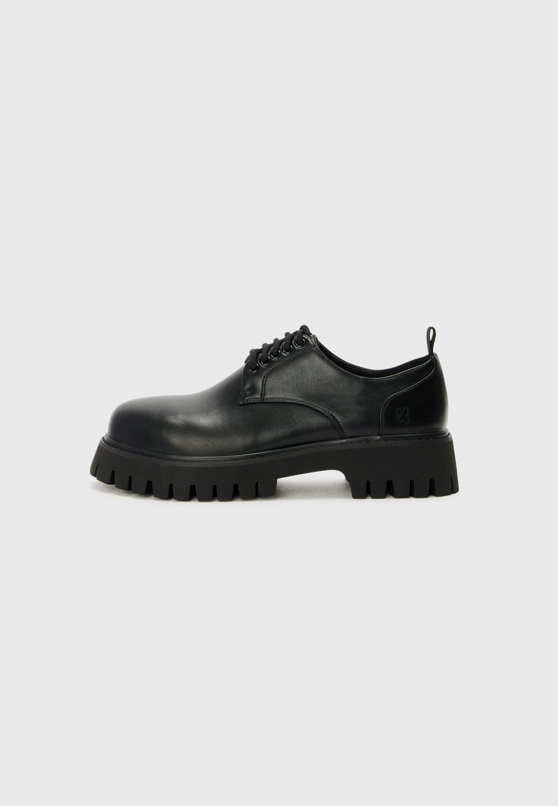 Chaussures en cuir noir à lacets avec un bout arrondi, semelle en caoutchouc texturé et une petite languette au niveau du talon. Comprend six œillets pour les lacets.