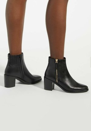 Black leather ankle boots with a block heel, featuring a pointed toe, side zippers, and vertical ribbed detail at the ankle.