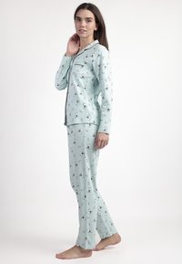 Conjunto de pijama de color azul claro hecho de material suave, con un patrón repetido de pequeños pingüinos. Incluye mangas largas y pantalones a juego.