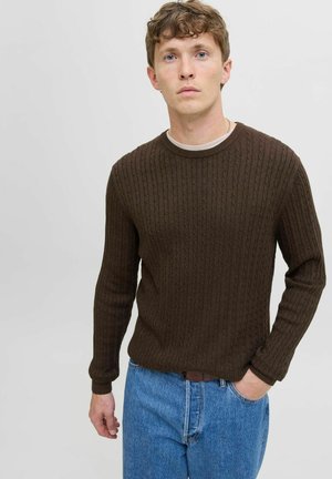 Brauner, gerippter Strickpullover mit rundem Ausschnitt und langen Ärmeln, kombiniert mit blauen Jeans. Die Textur ist glatt mit einem erhabenen Muster.