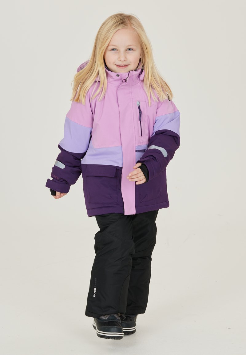 Lila und rosa isolierte Jacke mit Reißverschluss und Taschendetails, kombiniert mit schwarzen Hosen und Schuhen, entworfen für den Einsatz bei kaltem Wetter.