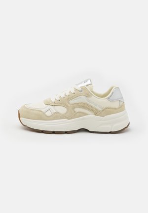 Beige Sneaker aus Wildleder und Mesh-Materialien, mit rundem Zehenbereich und weißen Schnürsenkeln. Silberne Akzente an der Ferse und der Zunge, strukturierte Gummisohle.