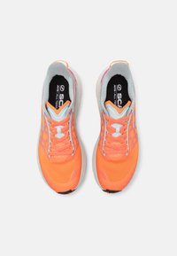 Oranje en roze sportchoenen met een textuur bovenkant, gaasdetails, witte veters en een gewatteerde witte zool. Logo zichtbaar op de tong.