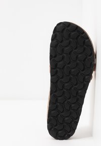 Černá gumová podešev s texturovaným vzorem připomínajícím překrývající se vlny, připojená k hnědé svrchní části. Plný design, tvarovaný pro pohodlí.