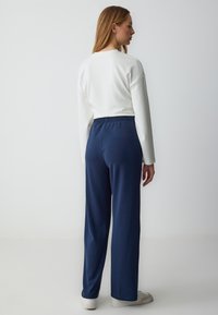 White long-sleeve top with a relaxed fit, paired with navy blue elastic-waist trousers. Smooth fabric, straight-leg design, minimal detailing.