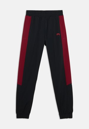 Pantalon de sport noir avec larges panneaux latéraux rouge foncé, taille élastique, bas de jambes élastiqués, poches avant et petit logo rouge sur la cuisse gauche.