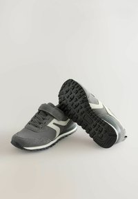 Ein Paar graue und weiße Sportschuhe mit schwarzen Profilsohlen, einer zeigt die Ansicht von oben und der andere die Unterseite.